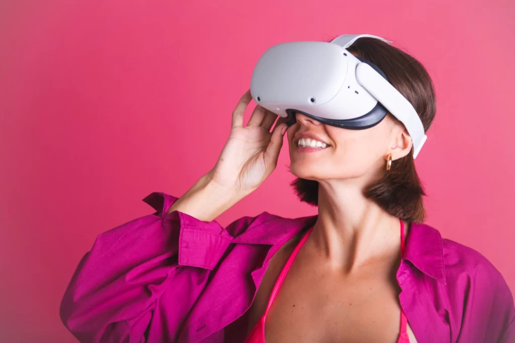 Beautiful fit tanned sporty woman in with virtual reality glasses on pink background